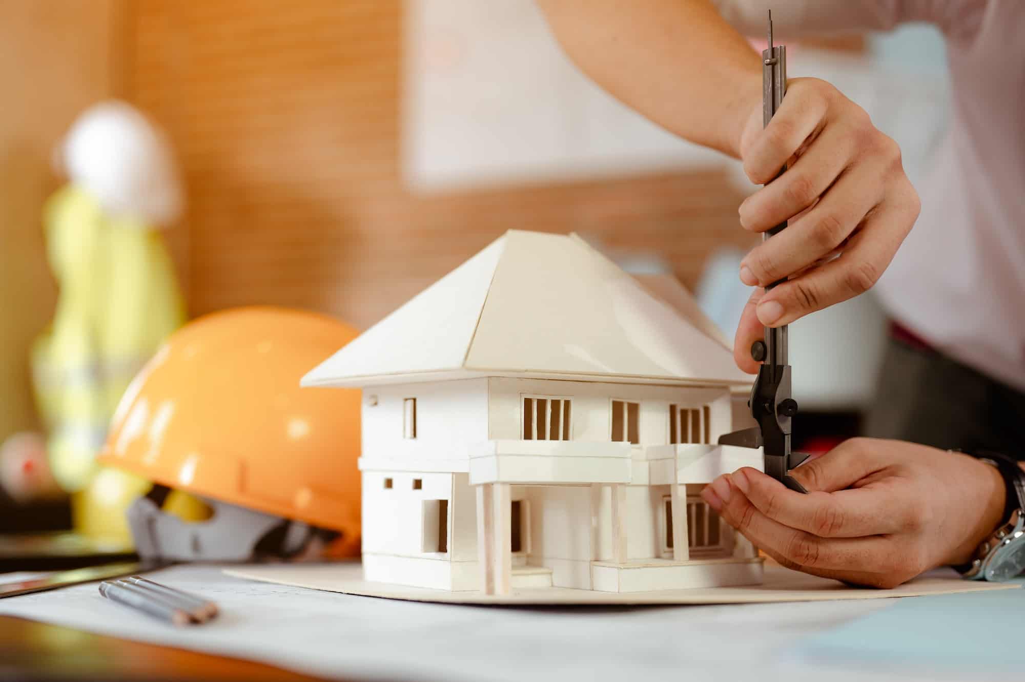 close-up-of-male-architect-hands-measuring-and-making-model-house-on-the-desk-at-sunset-.jpg